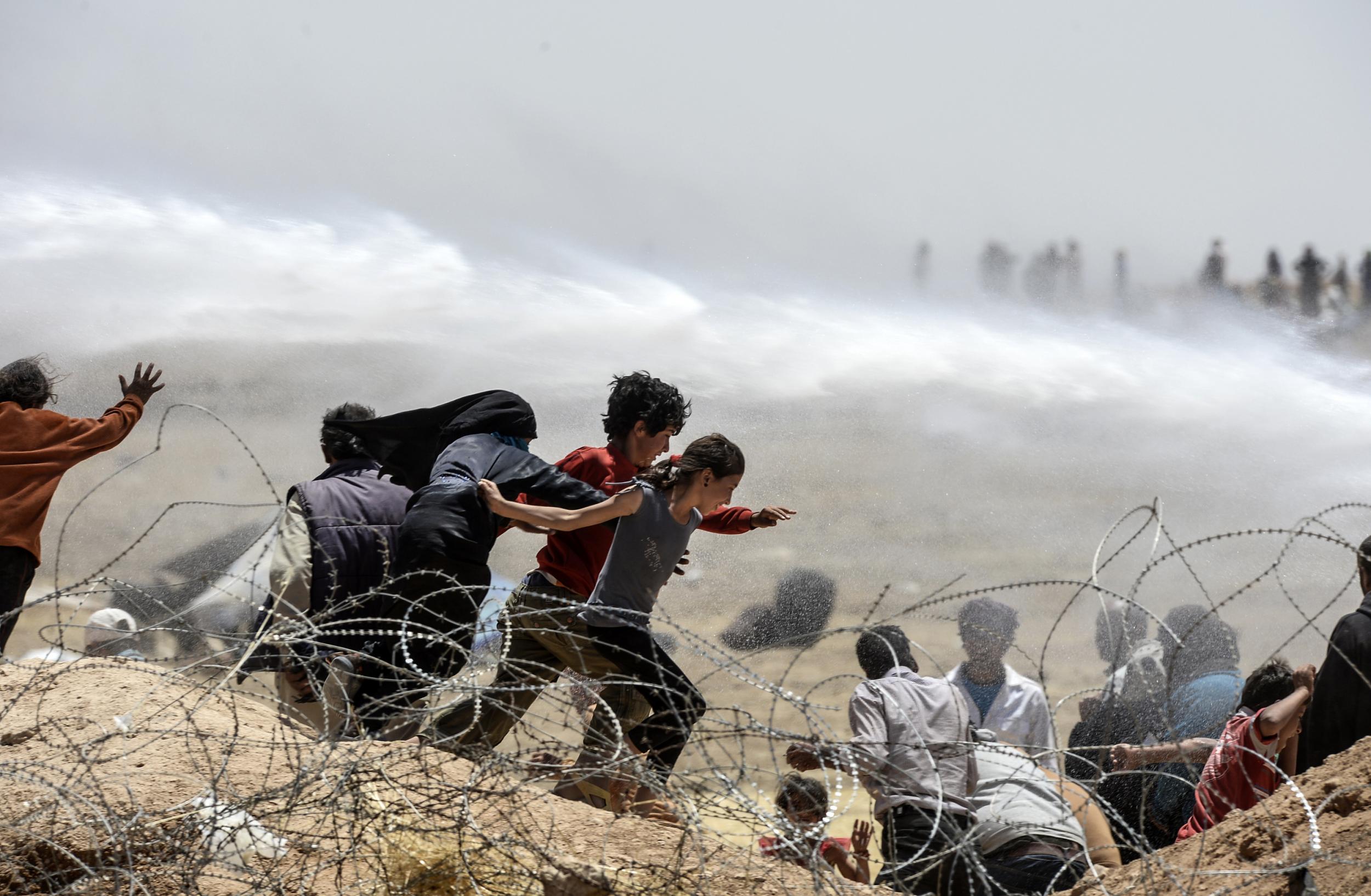 Syrian refugees run away as Turkish soldiers use water cannon to move them away from fences at the Turkish border near the Syrian town of Tal Abyad, at Akcakale in Sanliurfa province, on June 13, 2015