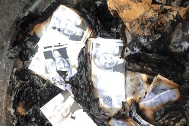 Notes bearing Theresa May's face are set alight outside the Home Office