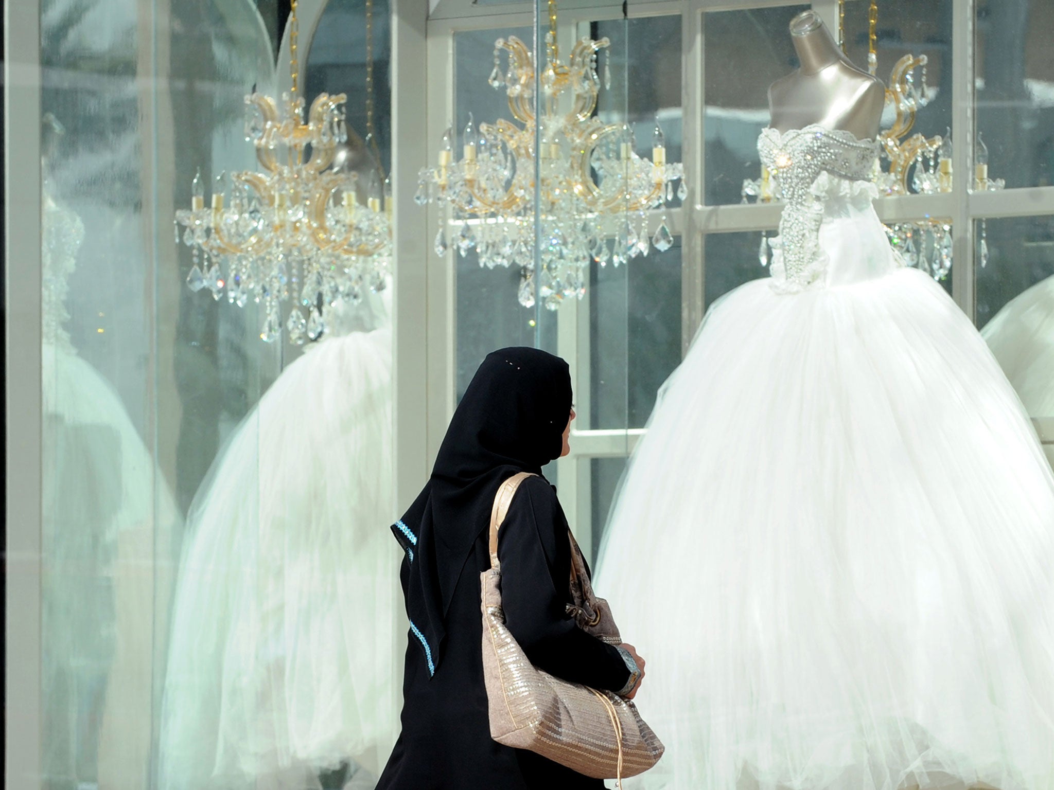 A Saudi woman walks past wedding dresses displayed in a shop window on February 4, 2013 at a mall in the Saudi capital Riyadh