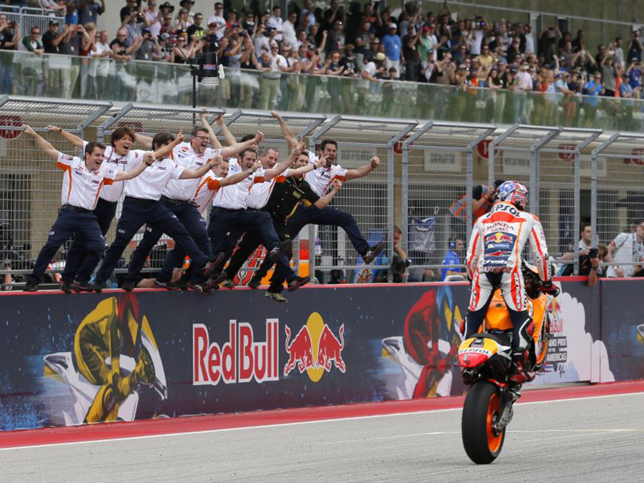 The Honda Racing team celebrate as Marc Marquez wheelies over the finish line to win the Grand Prix of America