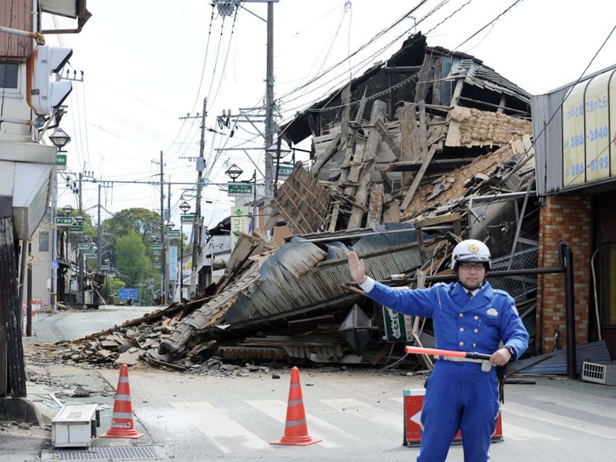 A police officer stands guard in front of a house destroyed by an earthquake in Mashiki, Kumamoto prefecture, southern Japan (Ryosuke Uematsu/Kyodo News/AP)