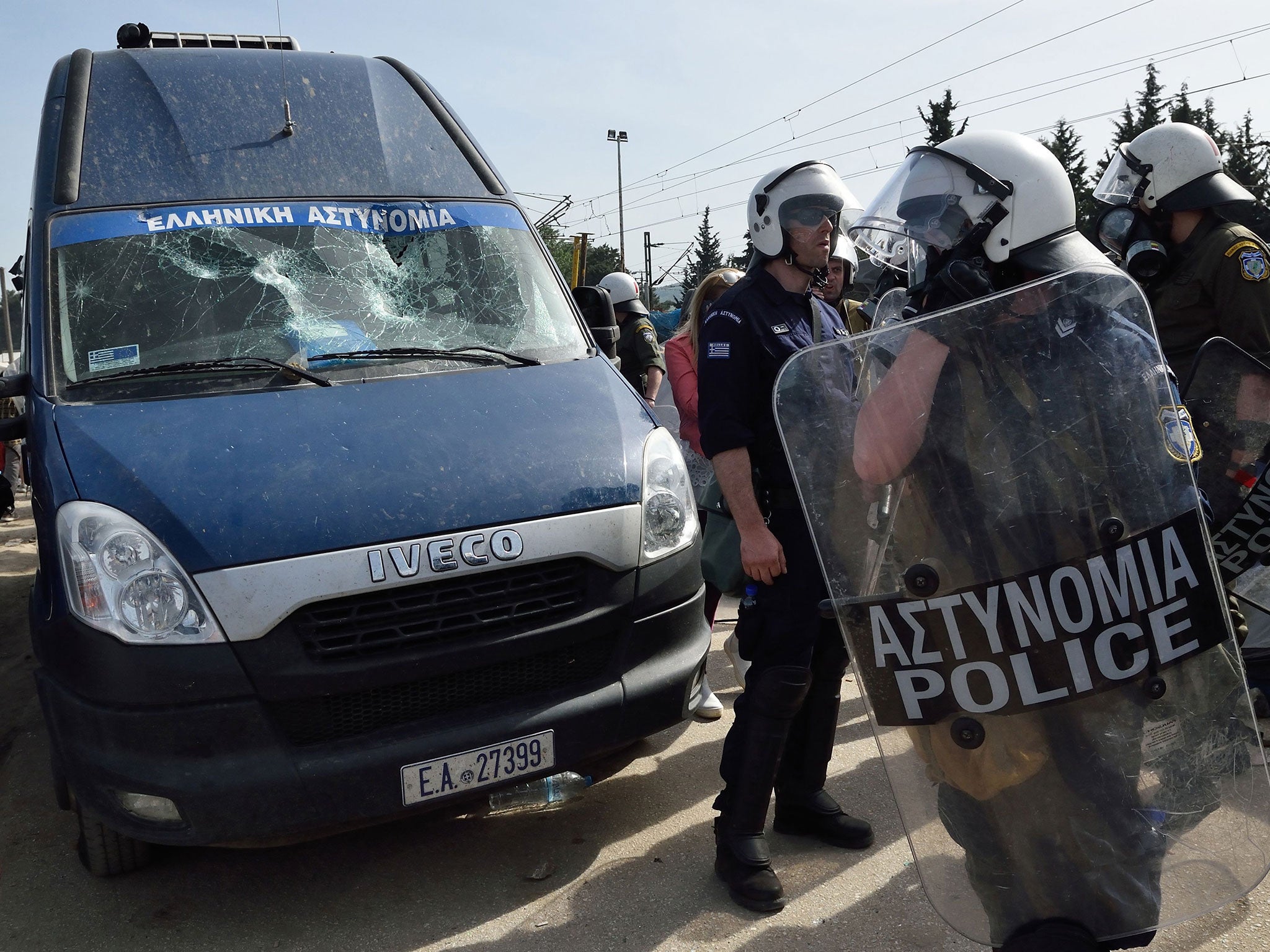 Greek police officers stand guard next to a police van that was involved in an accident that seriously injured a refugee at the Idomeni refugee camp on April 18, 2016.