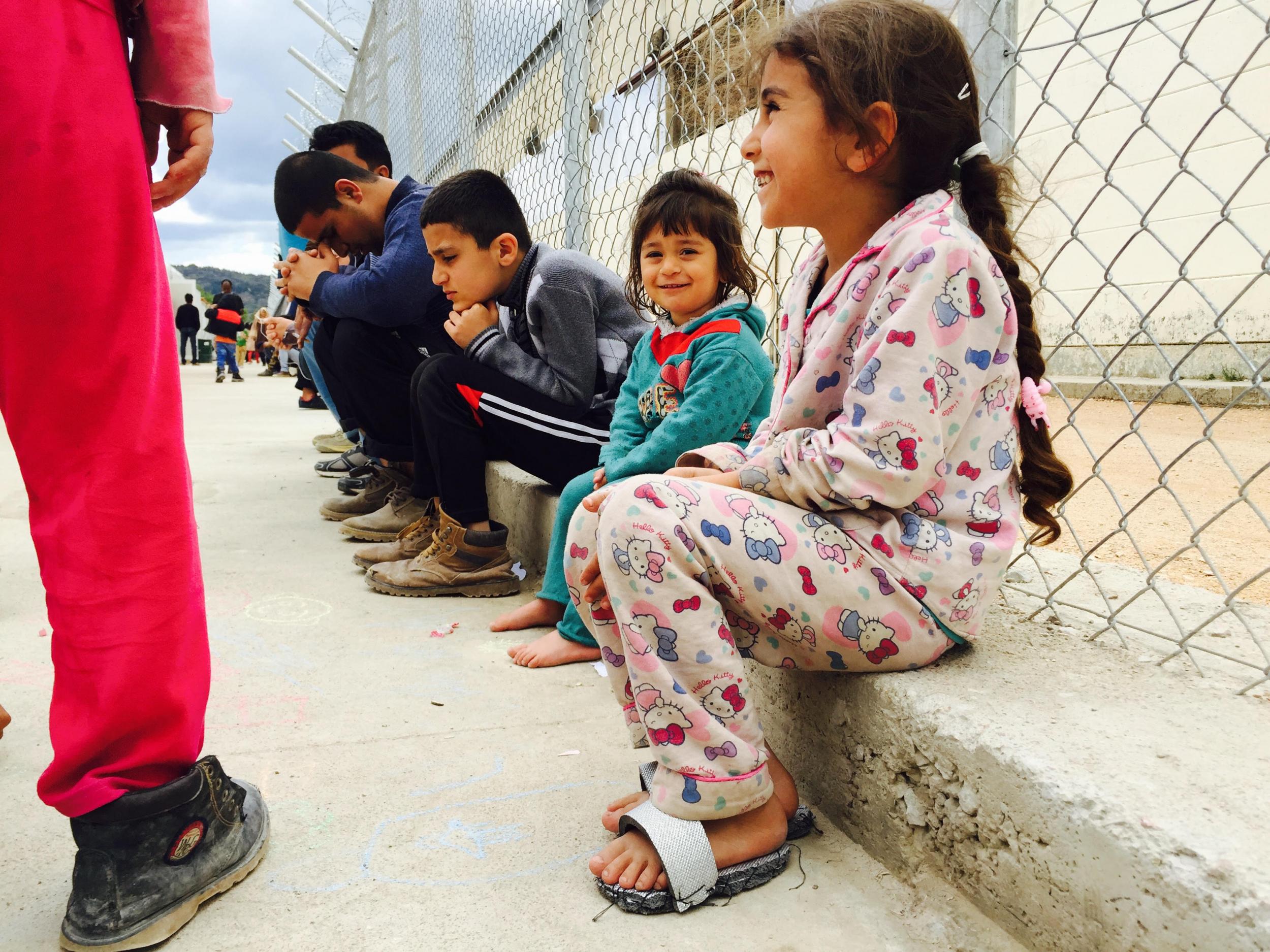 A young child – dressed in pyjamas and home-made sandals – smiles but others nearby appear sombre