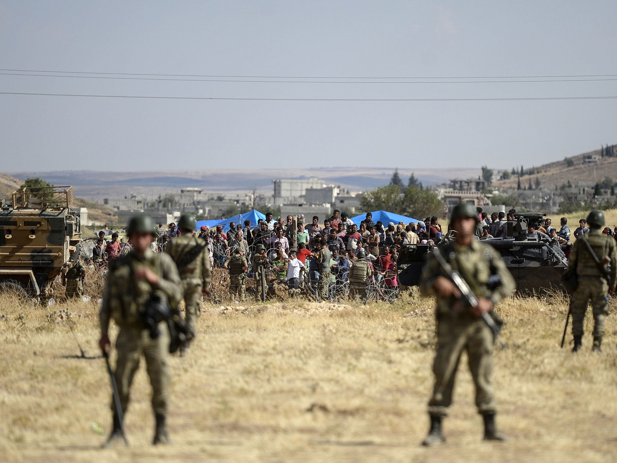 Turkish soldiers stand guard as Kurdish people wait for their relatives who wait near fences on the Syrian border on June 26, 2015 in Suruc, Turkey