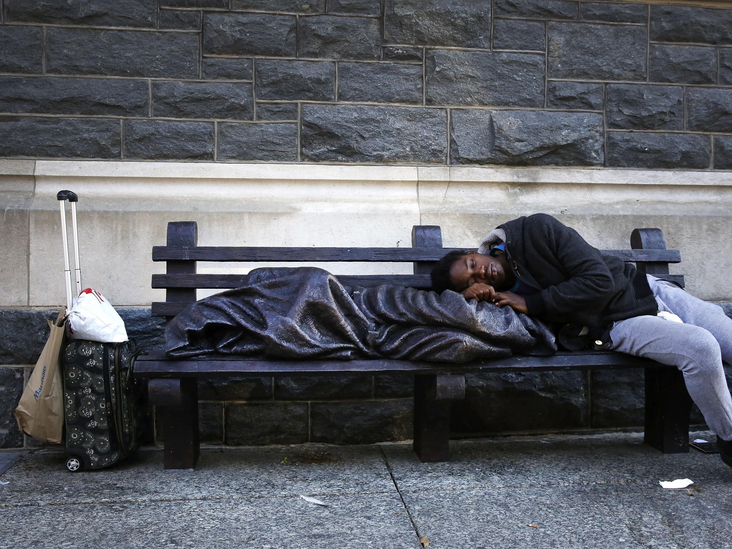 A man sleeps on a sculpture of a figure called 'Homeless Jesus' in front of the Archdiocese of Washington Catholic Charities offices in Washington DC, USA