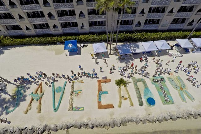 Sand sculpturists stand by their creations at the Cheeca Lodge Resort in Islamorada, Florida. People gathered on the resort's beach to create sand art letters to spell out "Save Earth" during an Earth Day event in the Florida Keys
