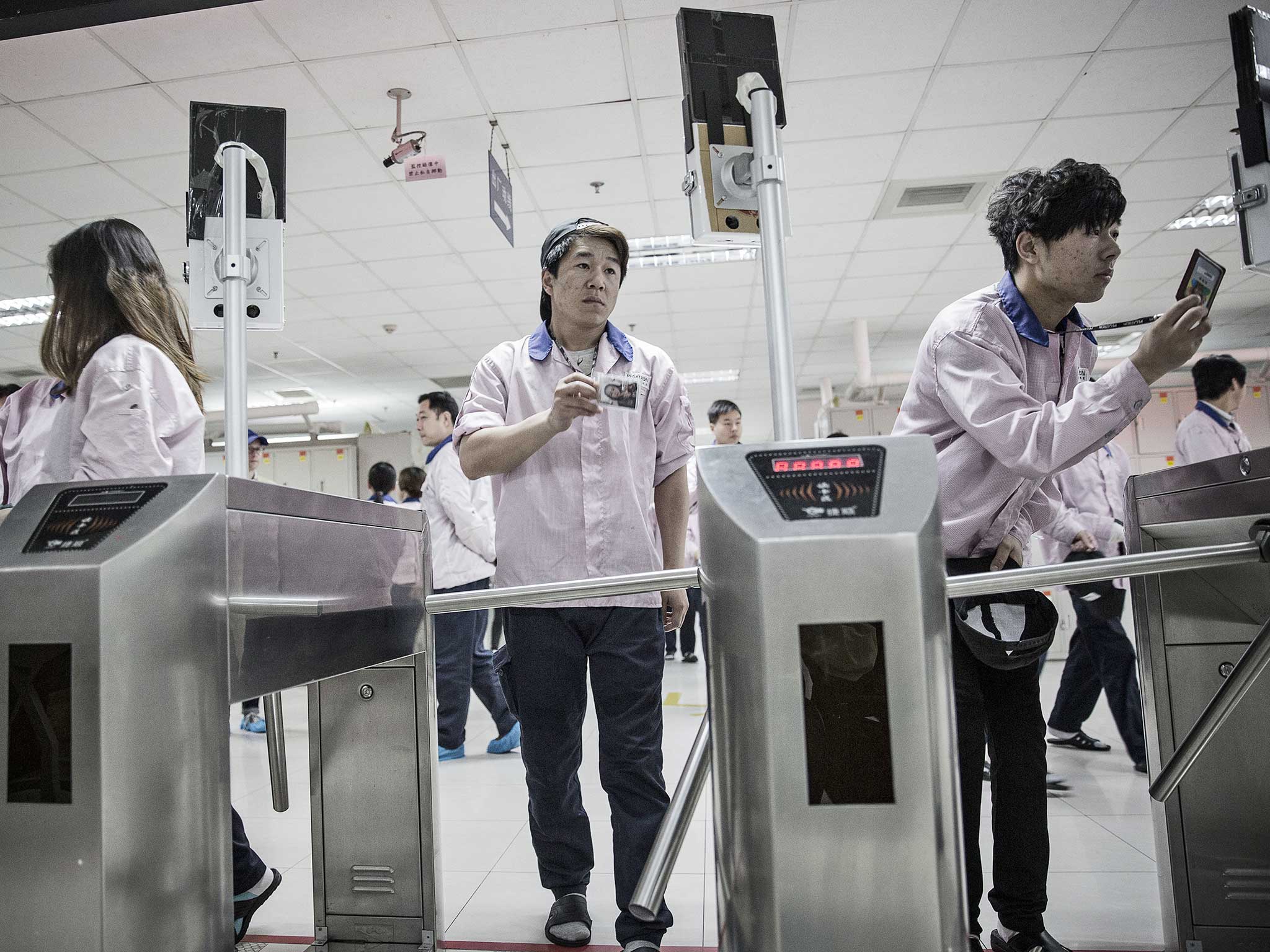 Employees look into facial recognition devices as they swipe their badges to enter the assembly line area at a Pegatron Corp. factory in Shanghai, China