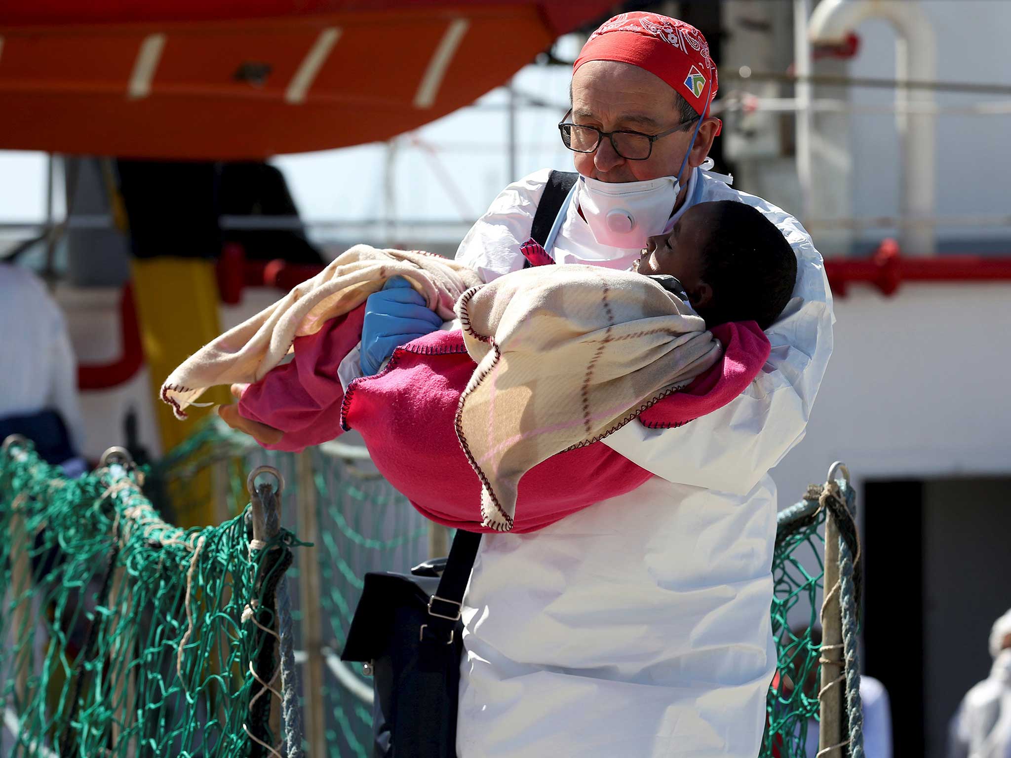 A doctor carries a child as refugees disembark from the Medecins Sans Frontieres (MSF) vessel at Pozzallo's harbour in Sicily, Italy