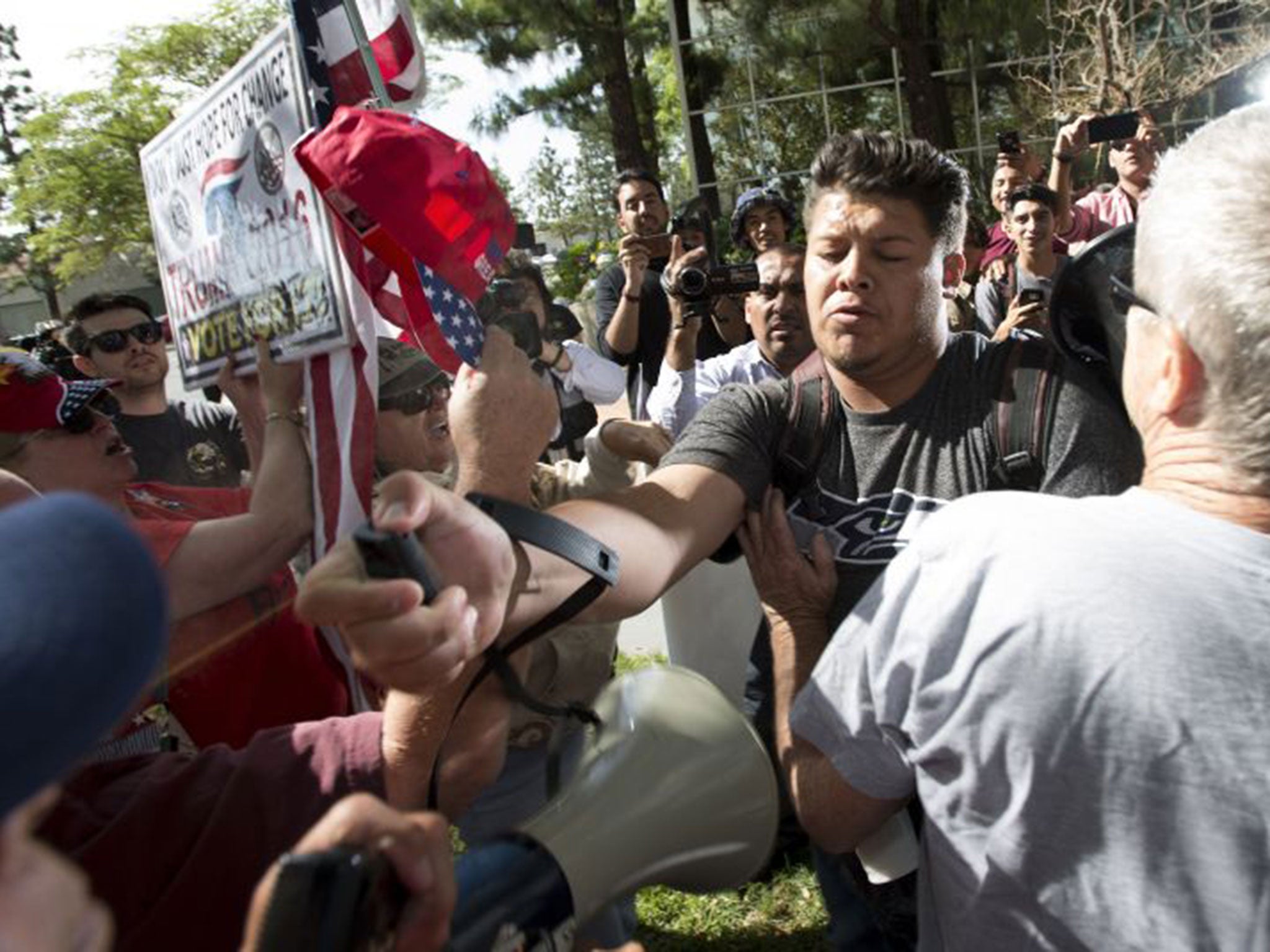 A man, center, sprays Republican presidential candidate Donald Trump supporters with pepper spray during a rally in front of the Anaheim City Hall