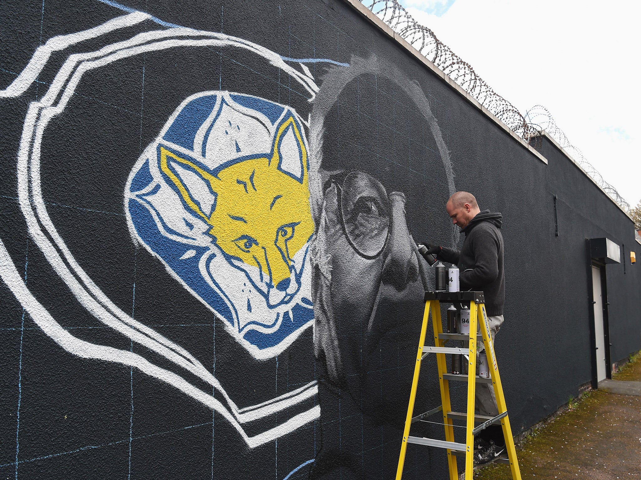 An artist paints Claudio Ranieri's face onto a wall in Leicester