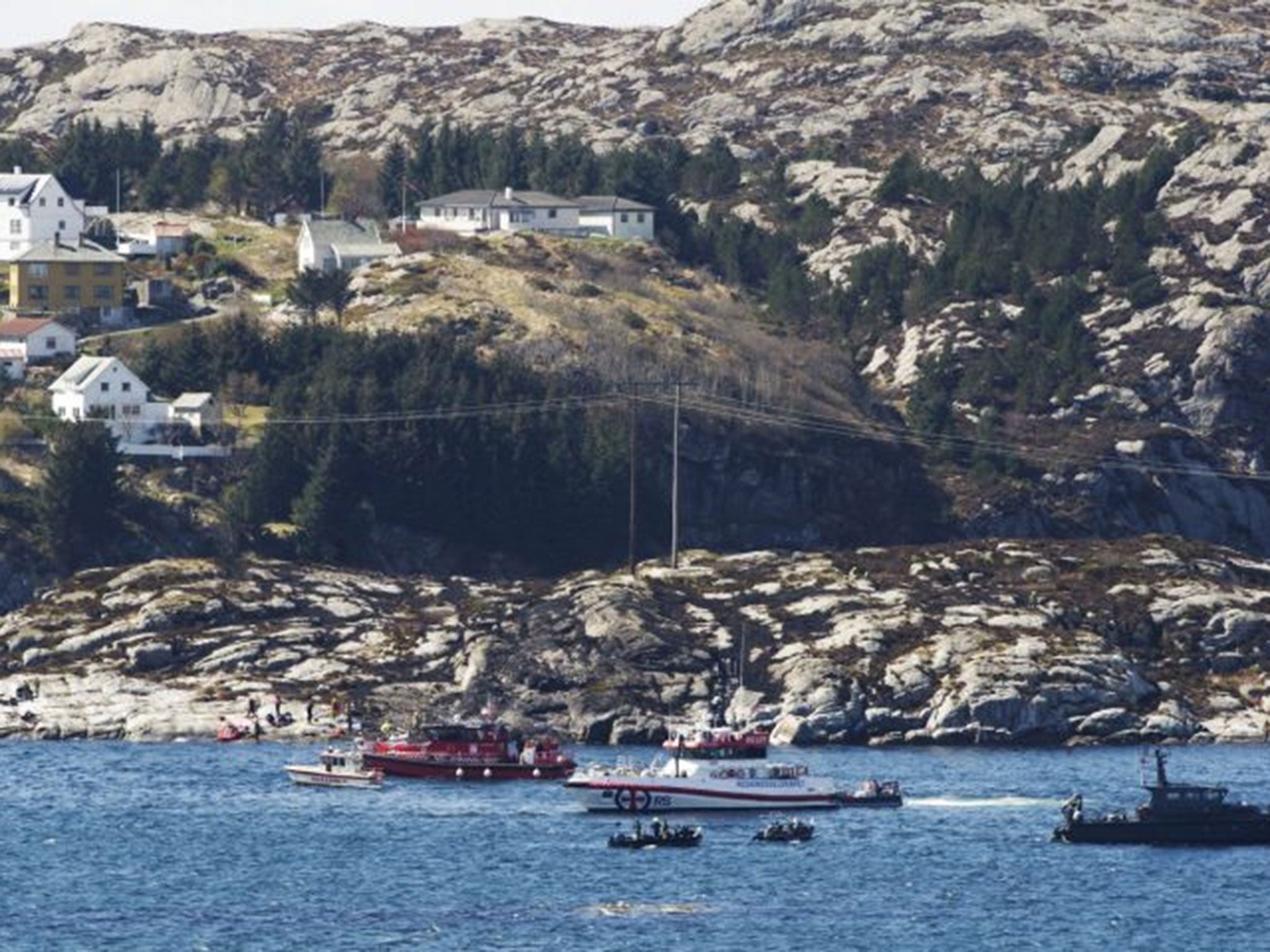 A search and rescue vessel patrols off the island of Turoey, near Bergen, Norway, as emergency workers on the shoreline attend the scene after a helicopter with 13 people on board crashed, Friday 29 April, 2016