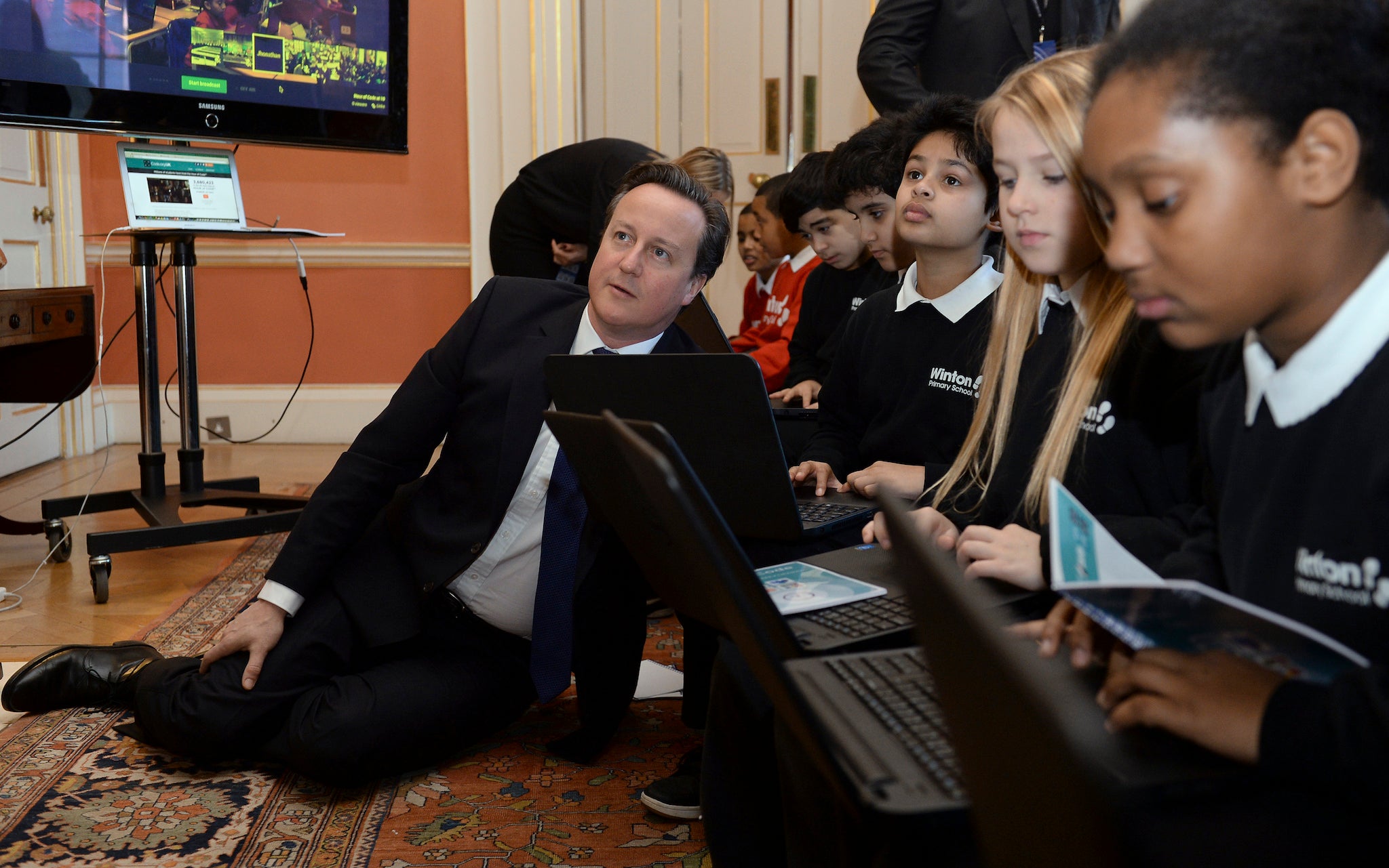 Britain's Prime Minister David Cameron sits on the floor as he joins students for "An Hour of Coding" at Number 10 Downing Street