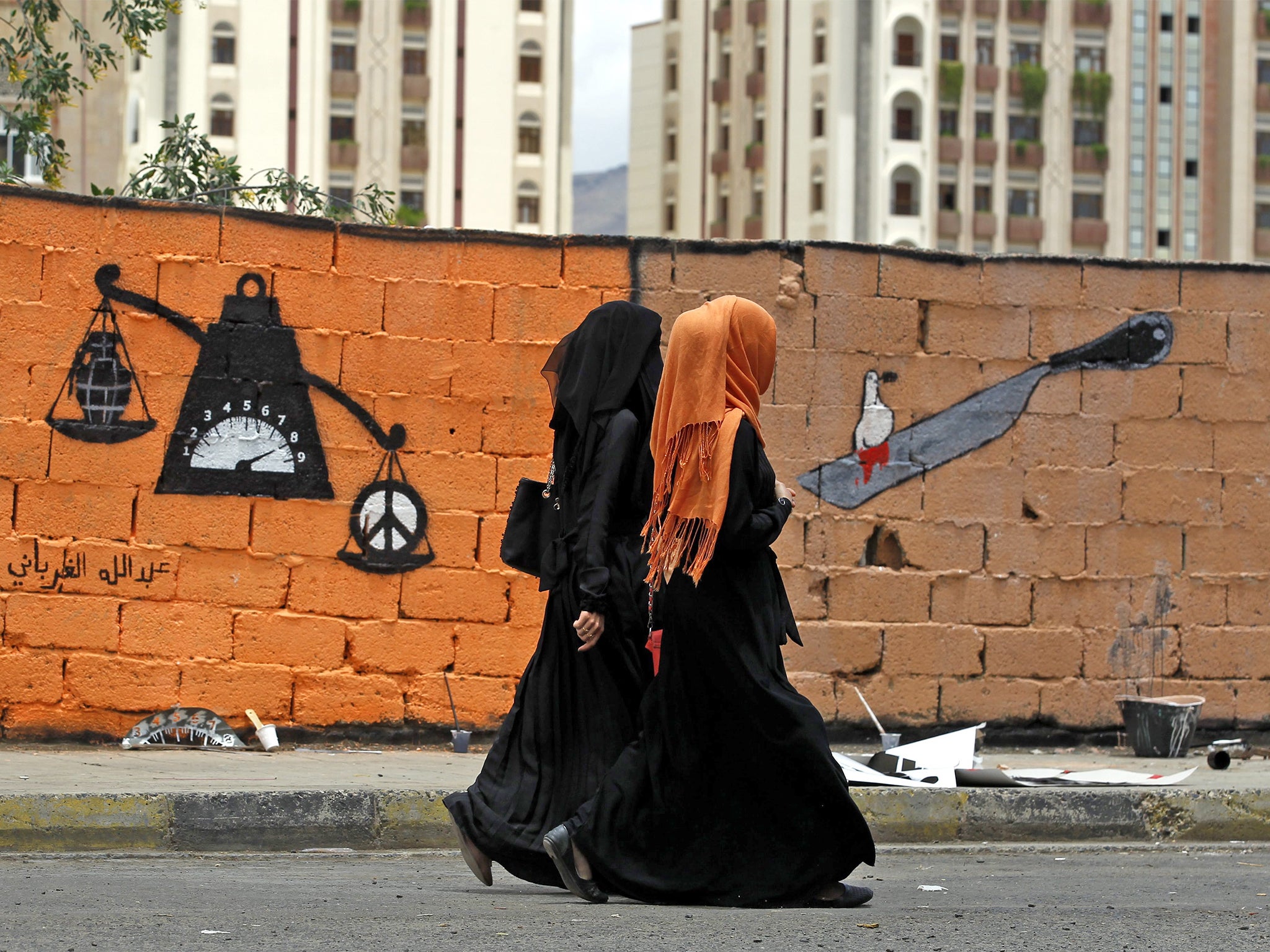 Yemeni women pass graffiti in support of peace in the war-affected country