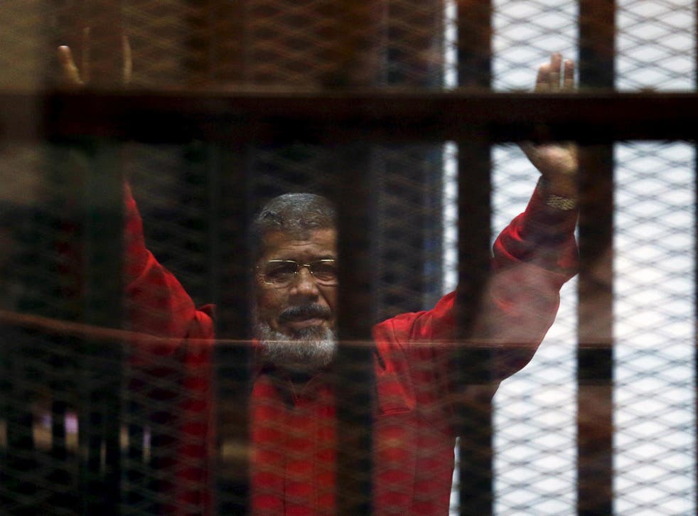 Deposed President Mohamed Mursi greets his lawyers from behind bars at a court wearing the red uniform of a prisoner sentenced to death