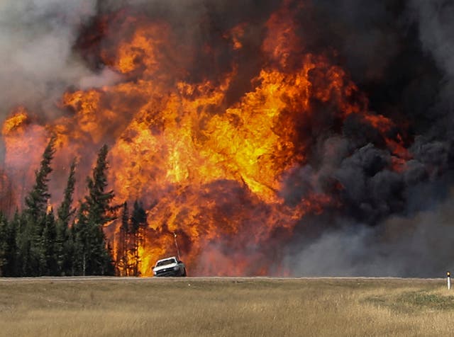 Smoke and flames from the wildfires erupt behind a car on the highway near Fort McMurray, Alberta, Canada