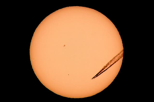 A jet airliner leaves a vapor trail as the planet Mercury is seen in the bottom left transiting across the face of the sun