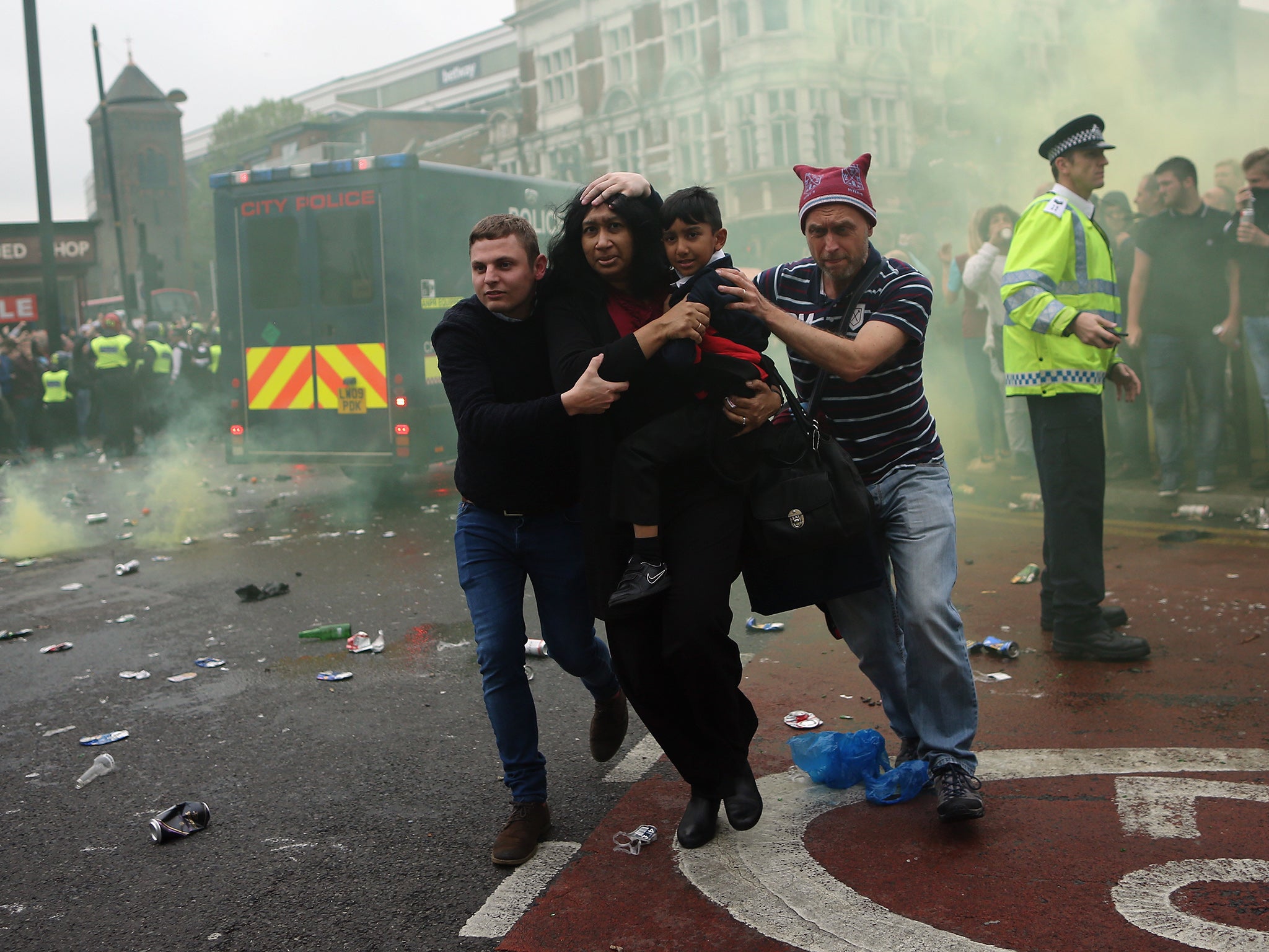 A woman and a child are helped past West Ham fans as people become violent and start throwing bottles at police outside the Boleyn Ground