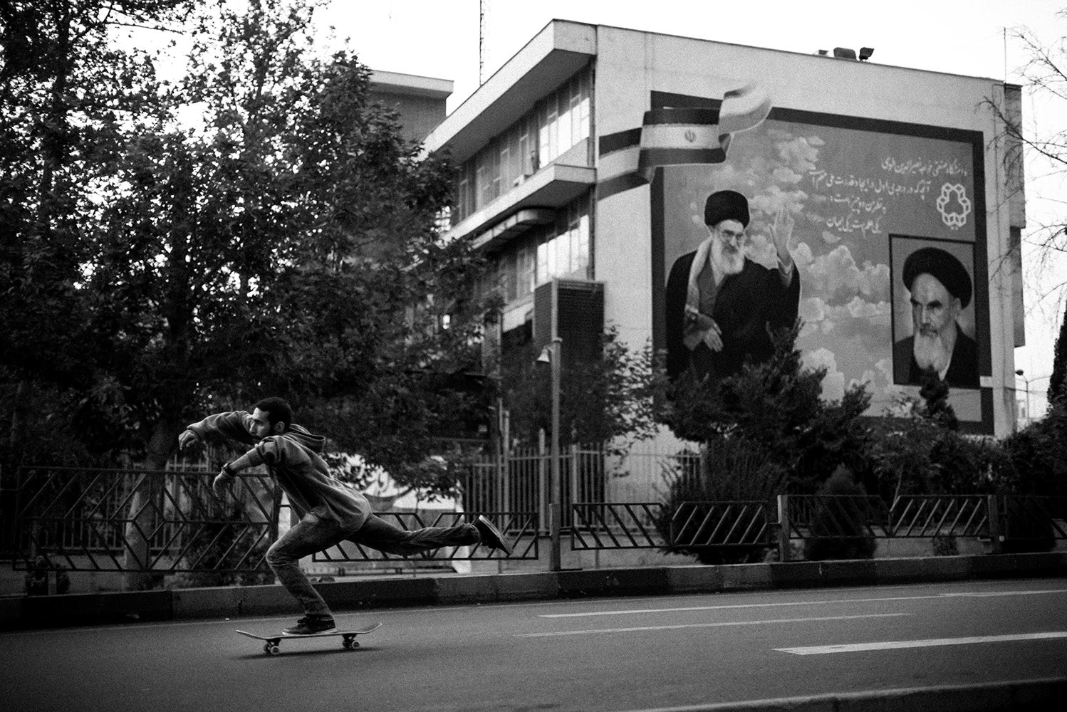 In Tehran, Erfan, 24, rides hurtles past the portraits of Khamenei (left), the Supreme Leader of the Islamic Republic of Iran since 1989, and his predecessor Khomeini (far right).
