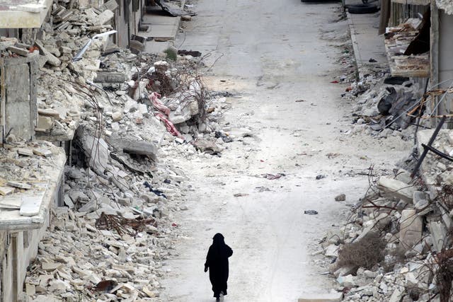 A woman walks past damaged buildings in the rebel-controlled area of Maaret al-Numan town in Idlib province