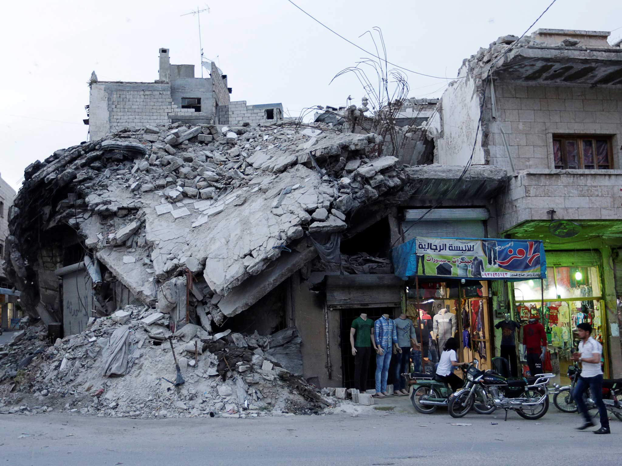 A clothing shop displays its merchandise beside a damaged building in the rebel-controlled area of Maaret al-Numan town in Idlib province, Syria