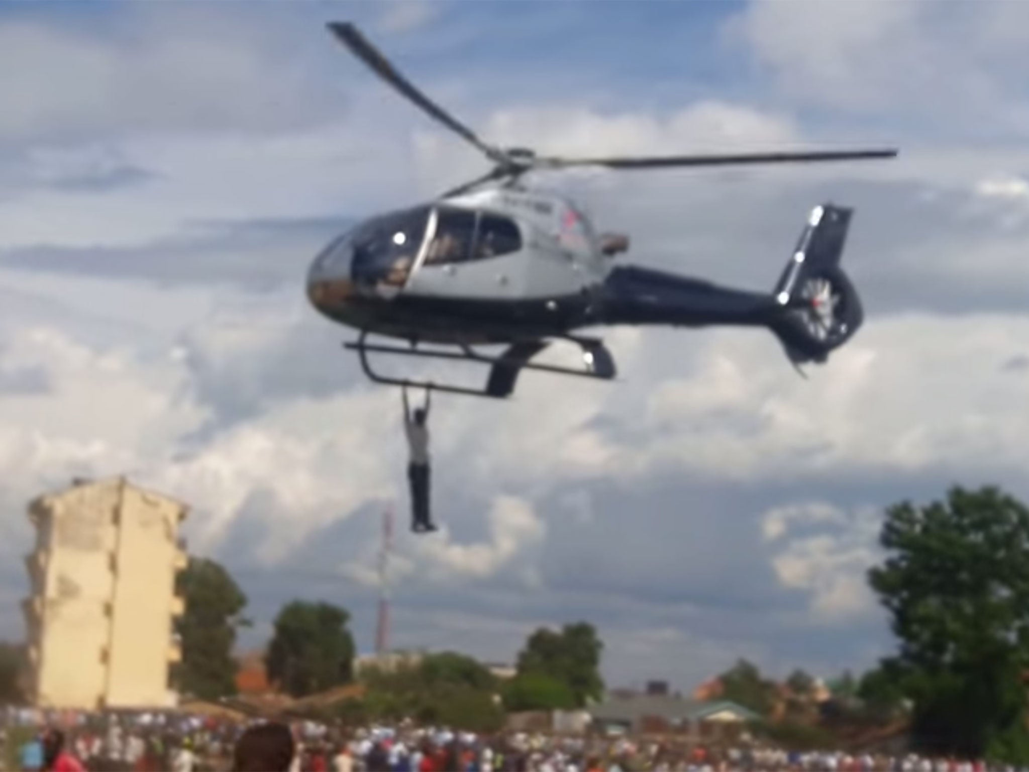 A man hangs on a chopper carrying the body of Jacob Juma and the bereaved family as it takes off from Bungoma Posta grounds
