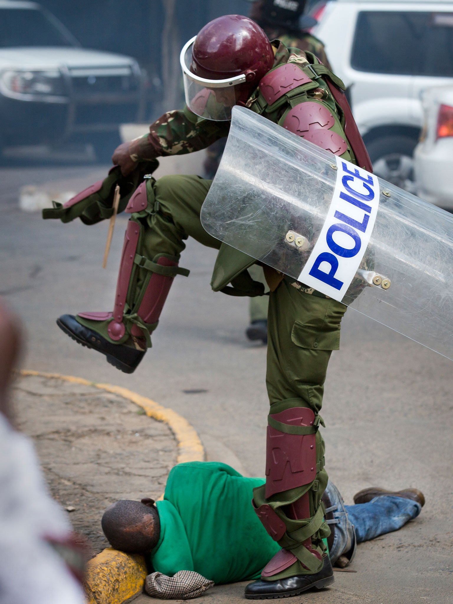 A Kenyan riot policeman repeatedly kicks a protester as he lies in the street after tripping over while trying to flee