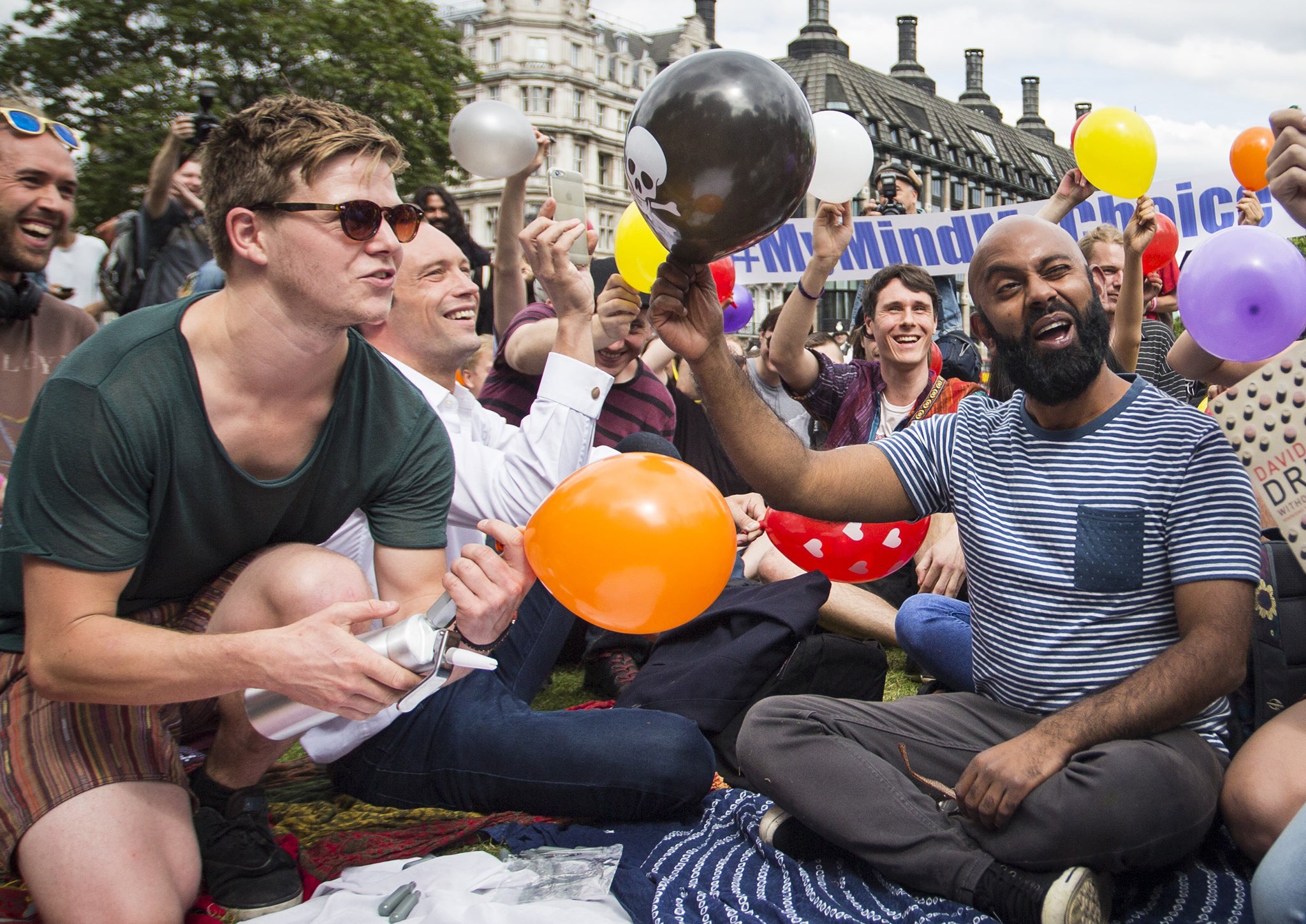 Dozens of protesters stage a mass inhalation of Nitrous Oxide, commonly known as laughing gas, outside the Houses of Parliament on August 1, 2015. The group of demonstrators inhaled the gas from balloons and chanted in protest at the government's proposed Psychoactive Substances Bill.