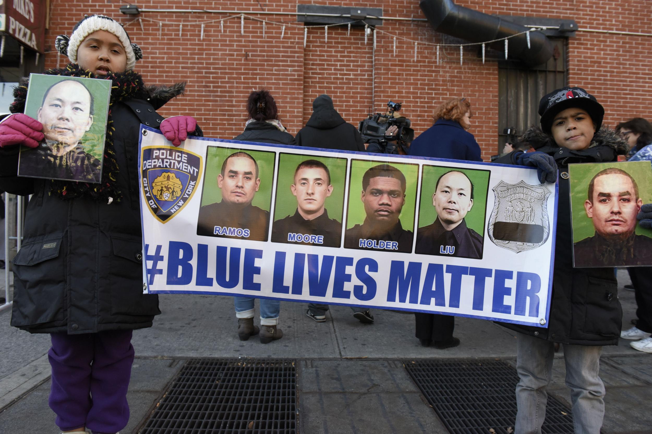 Two girls hold up pictures of slain NYPD officers Wenjian Liu and Rafael Ramos in December