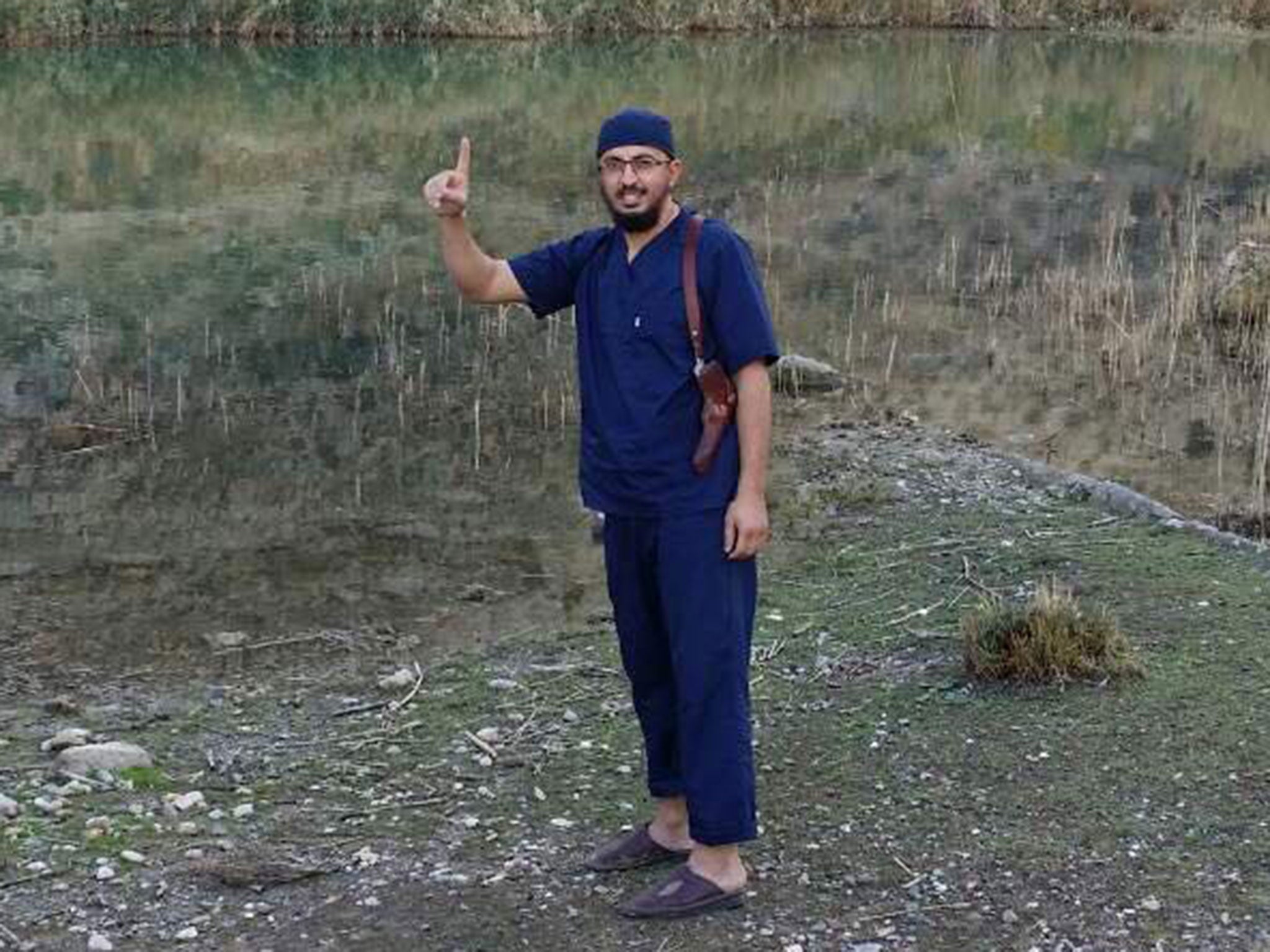 An image on Issam Abuanza's Facebook page shows him wearing doctors' scrubs and carrying a handgun in a holster, as he smiles and raises his index finger in the air in a gesture commonly associated with Isis