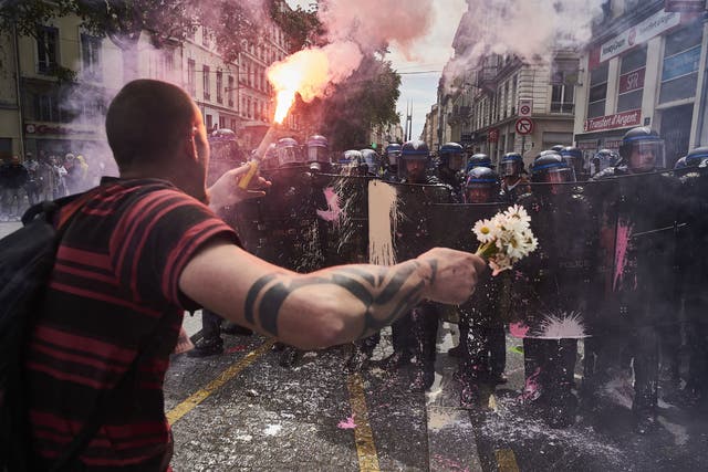 A man carrying flowers and a flare confronts a police barricade in Lyon