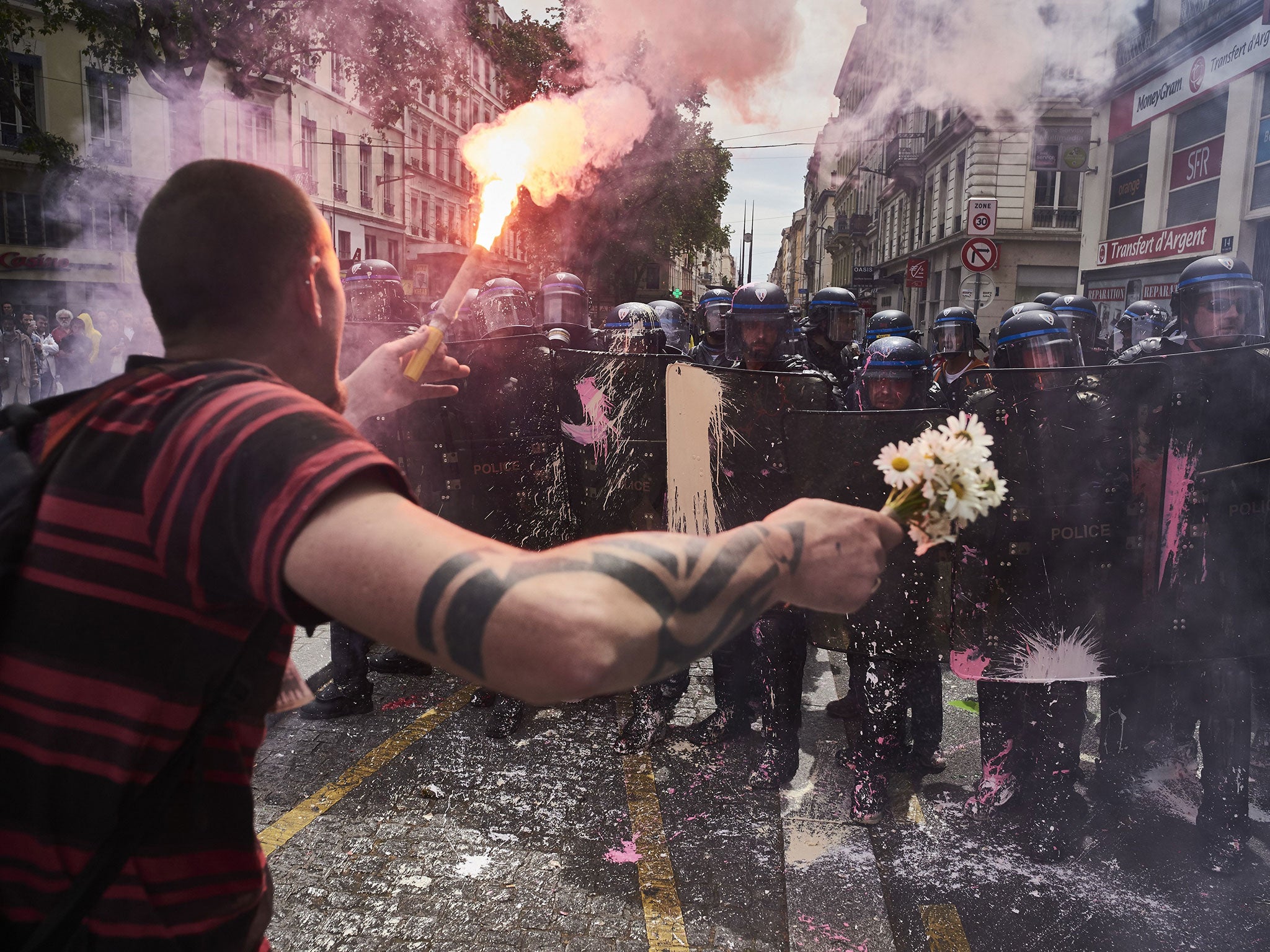 A man holds a bouquet of flowers and a torch as he faces riot police during a demonstration against the French government's planned labour reform on 26 May 2016 in Lyon, France