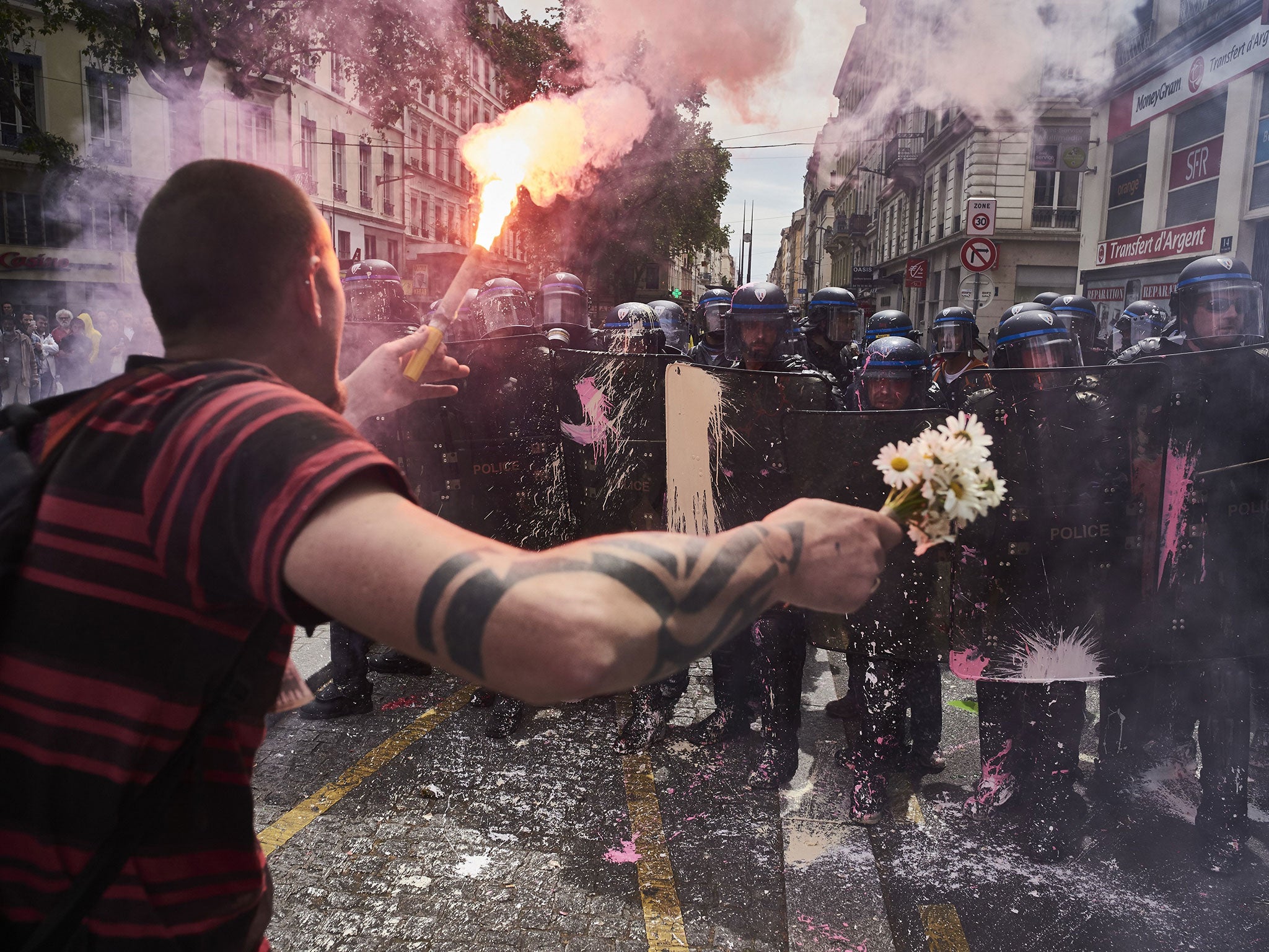 A man holds a bouquet of flowers and a torch as he faces riot police during a demonstration against the French government's planned labour reform, on 26 May, 2016 in Lyon, France