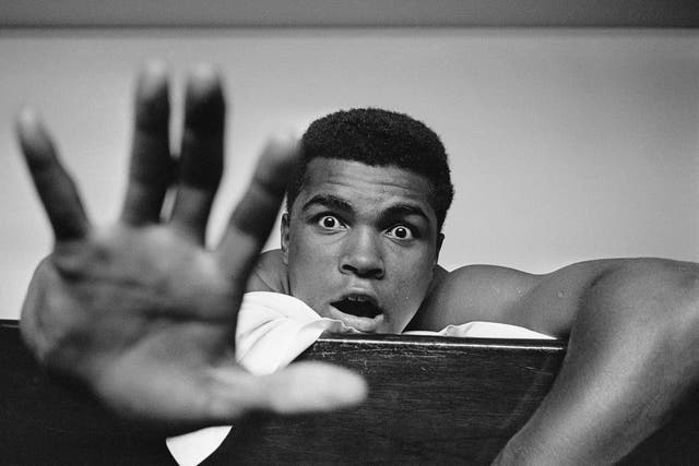 Muhammad Ali lying on his hotel bed in London, 27 May, 1963. He holds up five fingers in a prediction of how many rounds it will take him to knock out British boxer Henry Cooper