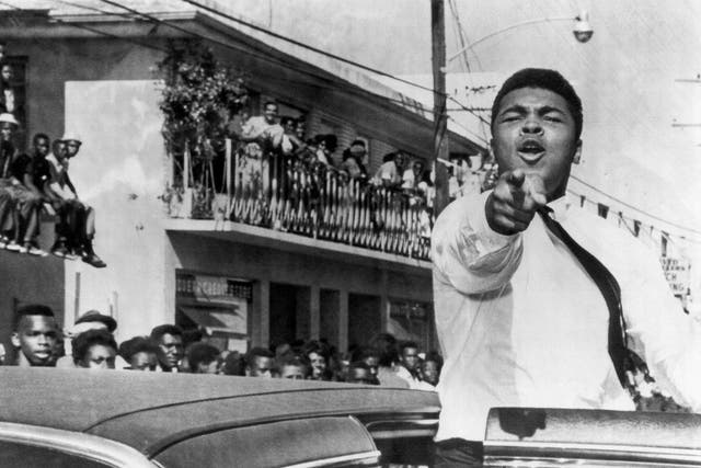 Muhammad Ali points at the camera from an open car door as he takes part in a pre-football game parade in December 1963