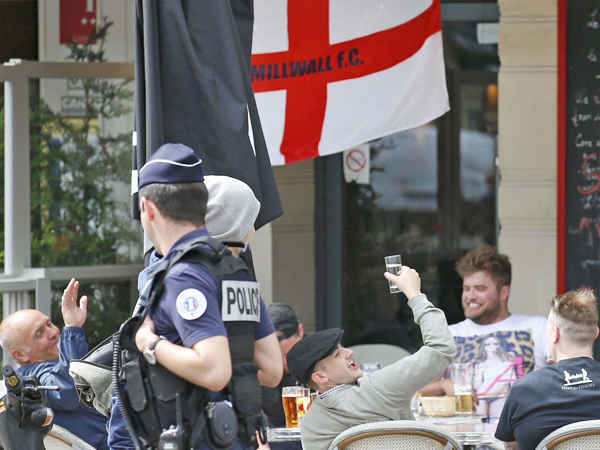 Enland fans seated at a cafe terrace, wave to a passing police patrol in Lille