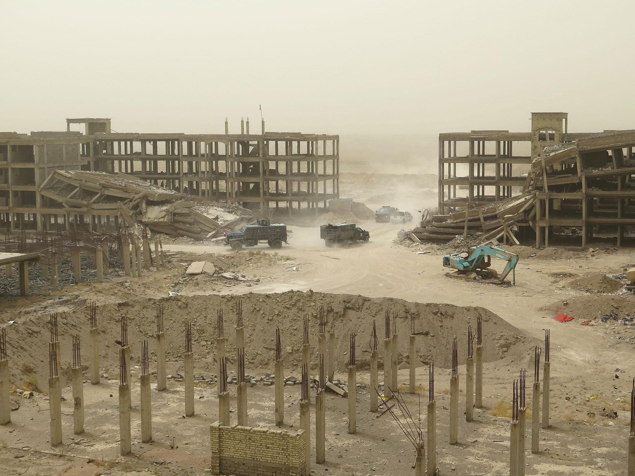 Iraqi forces vehicles drive past damaged buildings in Fallujah's southern Hayakel neighbourhood