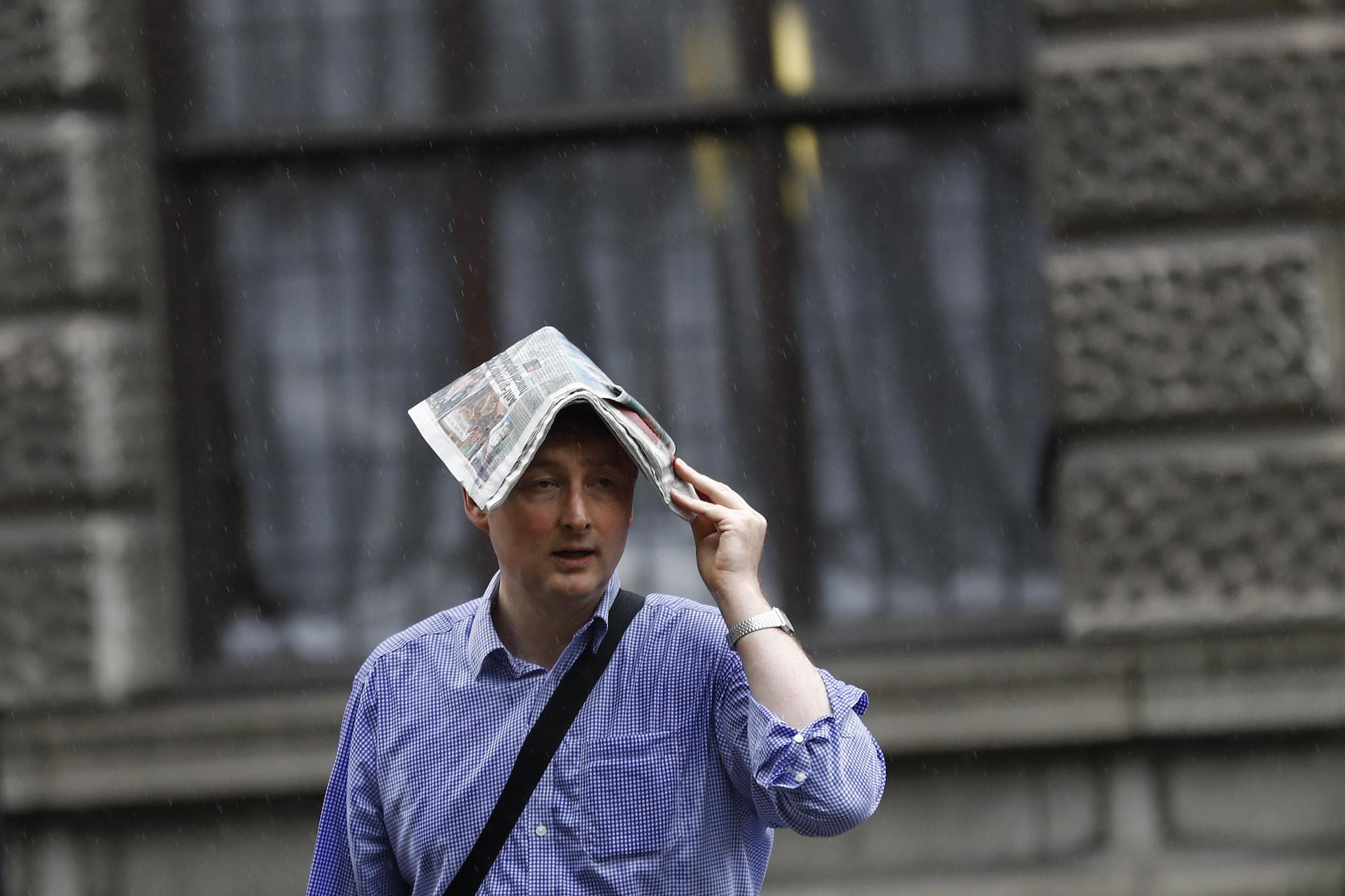 A man covers his head with a newspaper during heavy rain in London, Britain June 20, 2016