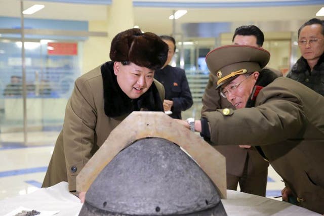 North Korean leader Kim Jong Un looks at a rocket warhead tip after a simulated test of atmospheric re-entry of a ballistic missile, at an unidentified location