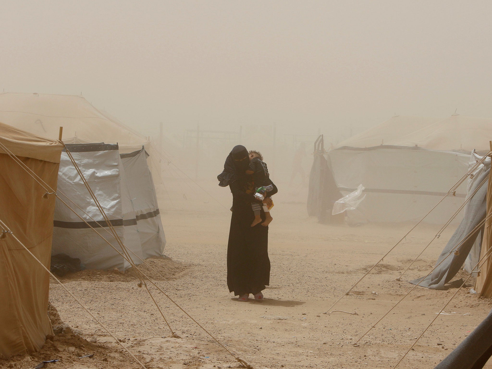 A woman, who fled from Fallujah carries her child during a dust storm at a refugee camp in Amiriyat al Fallujah in Iraq on June 16, 2016