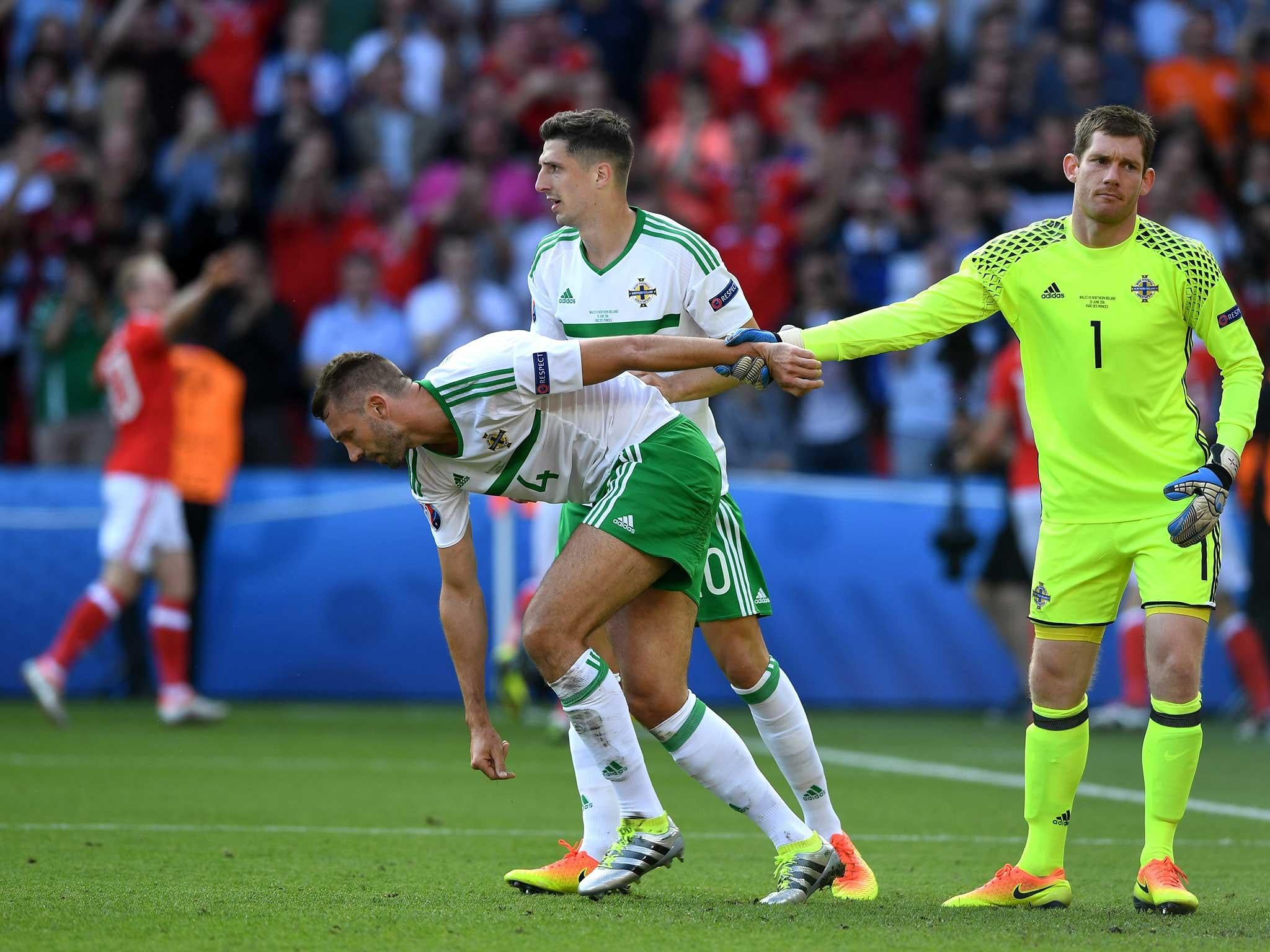 Gareth McAuley is consoled by his team-mates after scoring an own-goal against Wales