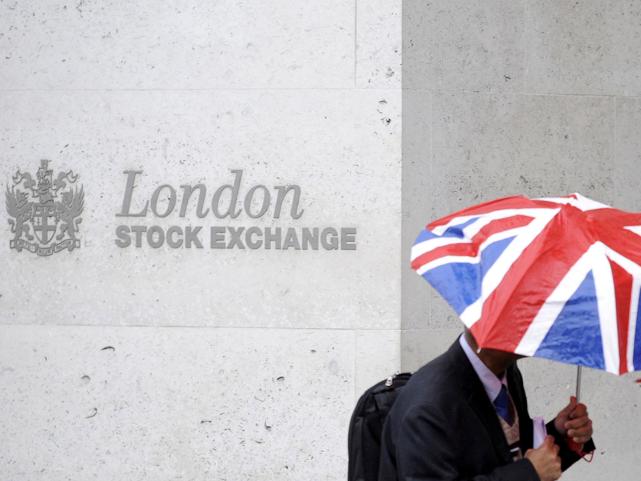 A worker shelters from the rain as he passes the London Stock Exchange in the City of London at lunchtime