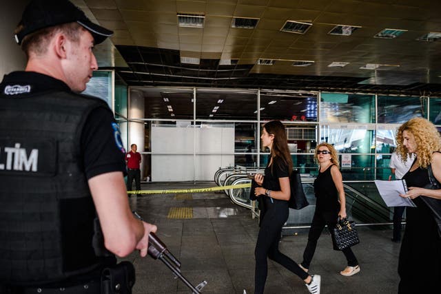 A Turkish anti-riot police officer stands guard as people walk past near the explosion site on 29 June, 2016 at Ataturk airport International arrival terminal in Istanbul, a day after a suicide bombing and gun attack targeted Istanbul's airport, killing at least 36 people