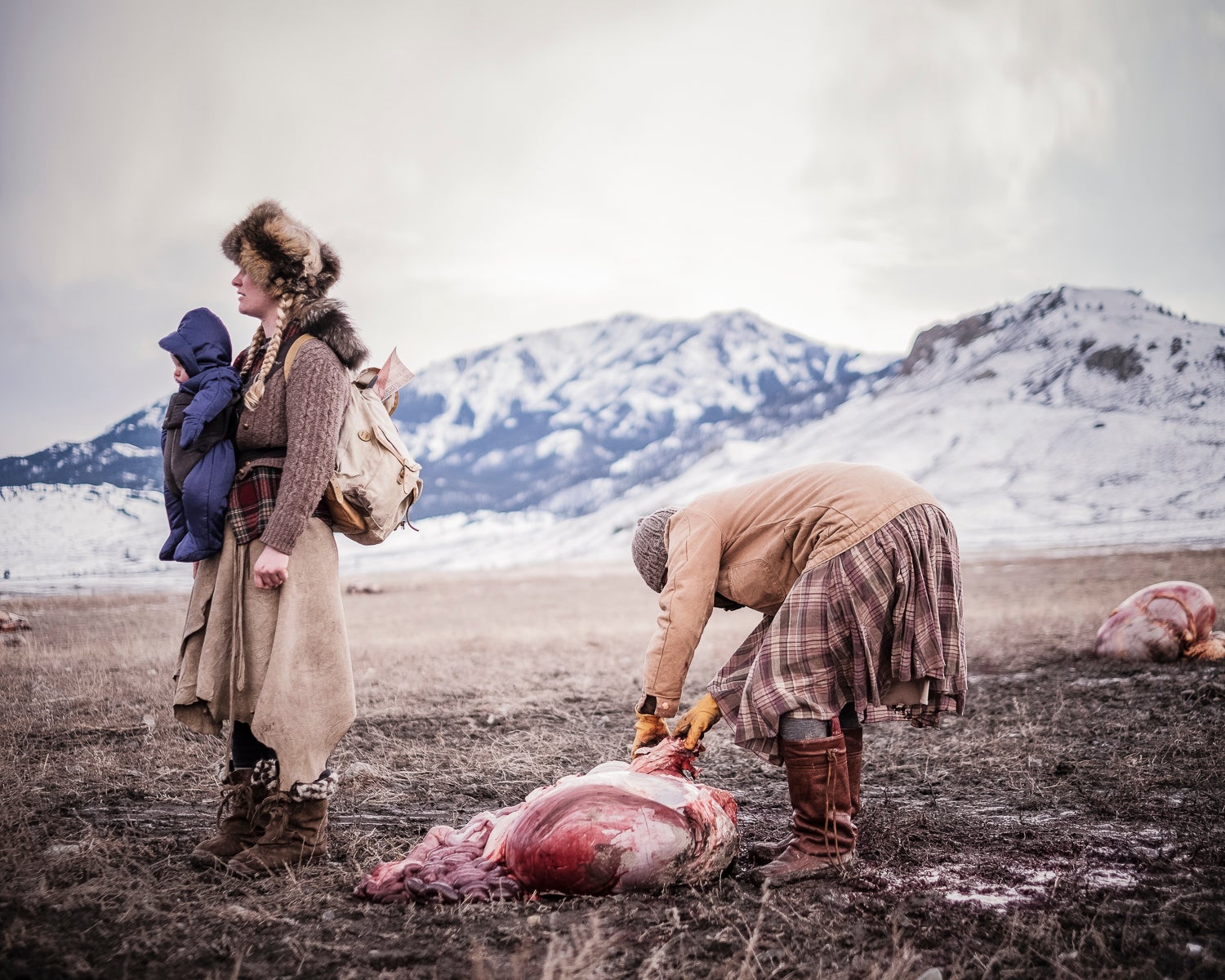 Ania pulls buffalo fat from a gut pile as Epona waits with backpack. Buffalo Bridge will occasionally be gifted a hide, bones, and even organs like the heart and liver