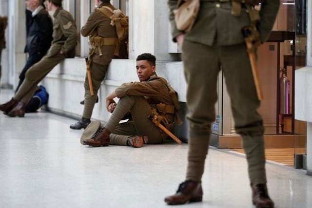 Volunteer actors dressed in World War I army fatigues stand silently in Waterloo station