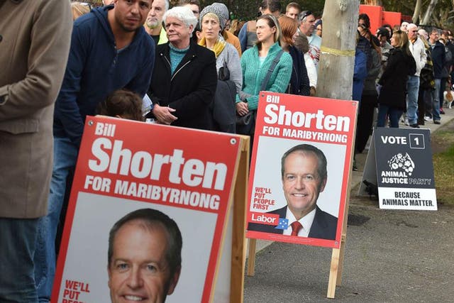 People wait in a queue next to posters of candidate Labor Party leader Bill Shorten, before casting their votes at a polling station in Melbourne