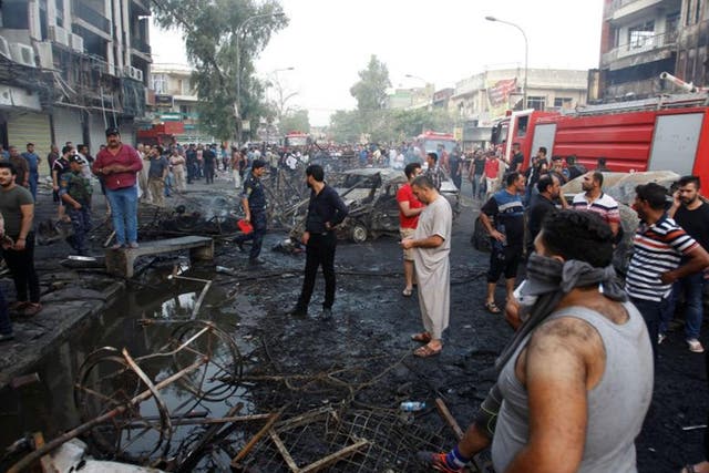 People gather at the site of an Isis suicide car bomb in Baghdad
