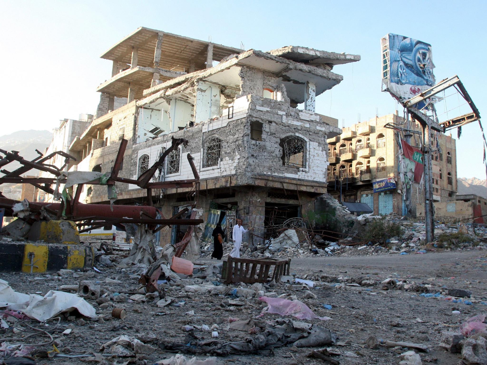 People walk past a building destroyed during fighting in Yemen's southwestern city of Taiz