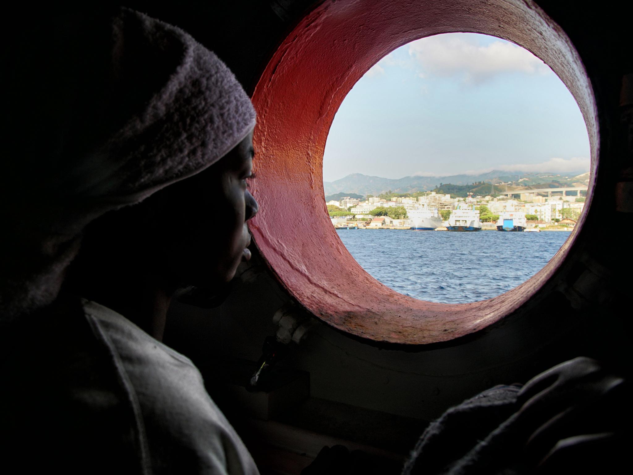 A woman looks out of the porthole from aboard the 'Aquarius' rescue vessel after arriving in Sicily, Italy, on Sunday June 25, 2016.  A group of more than 650 migrants arrived at port in Messina, Sicily, after being rescued from the Mediterranean Sea in June 2016