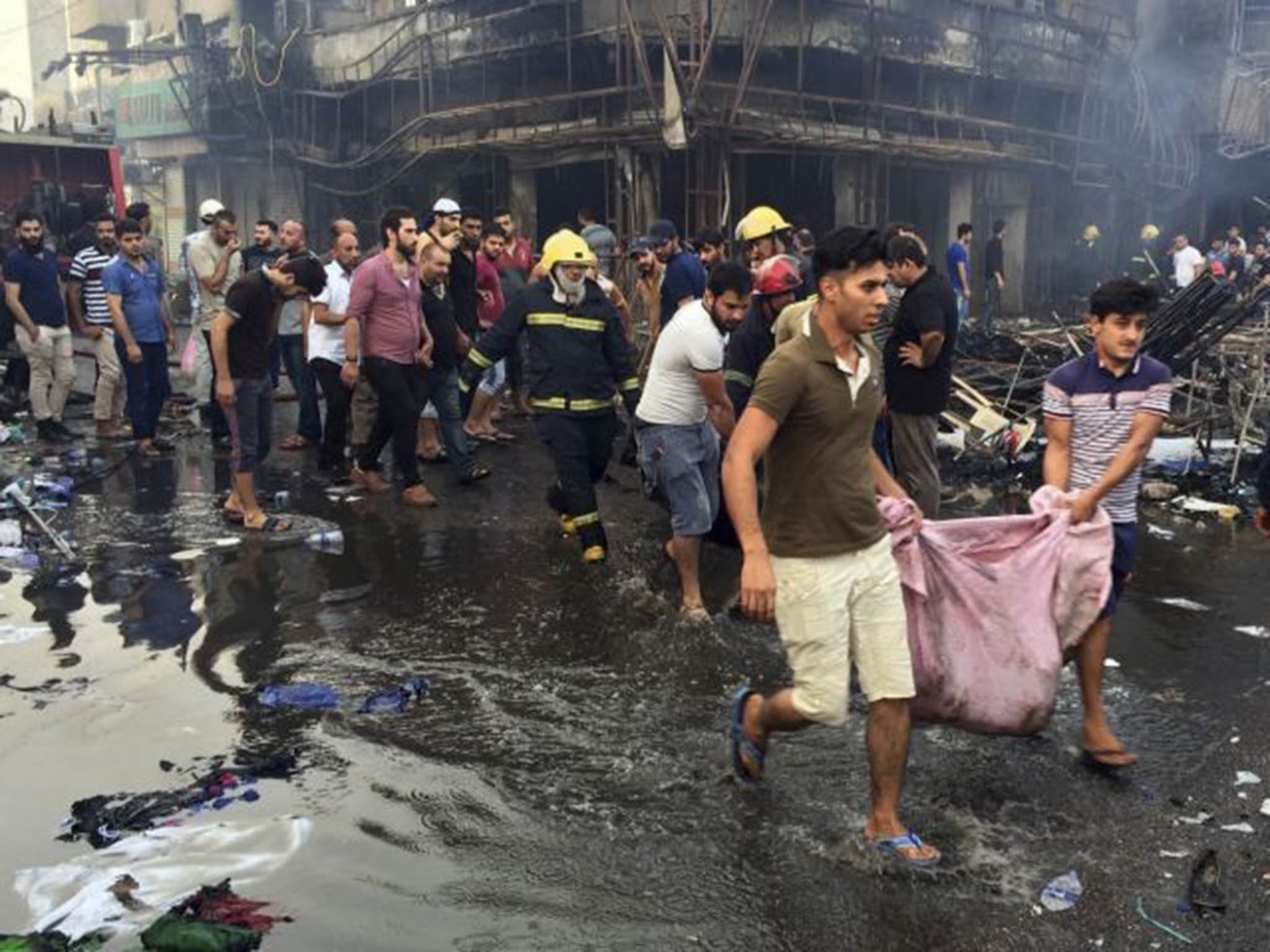 Iraqi firefighters and civilians work together to evacuate bodies of victims