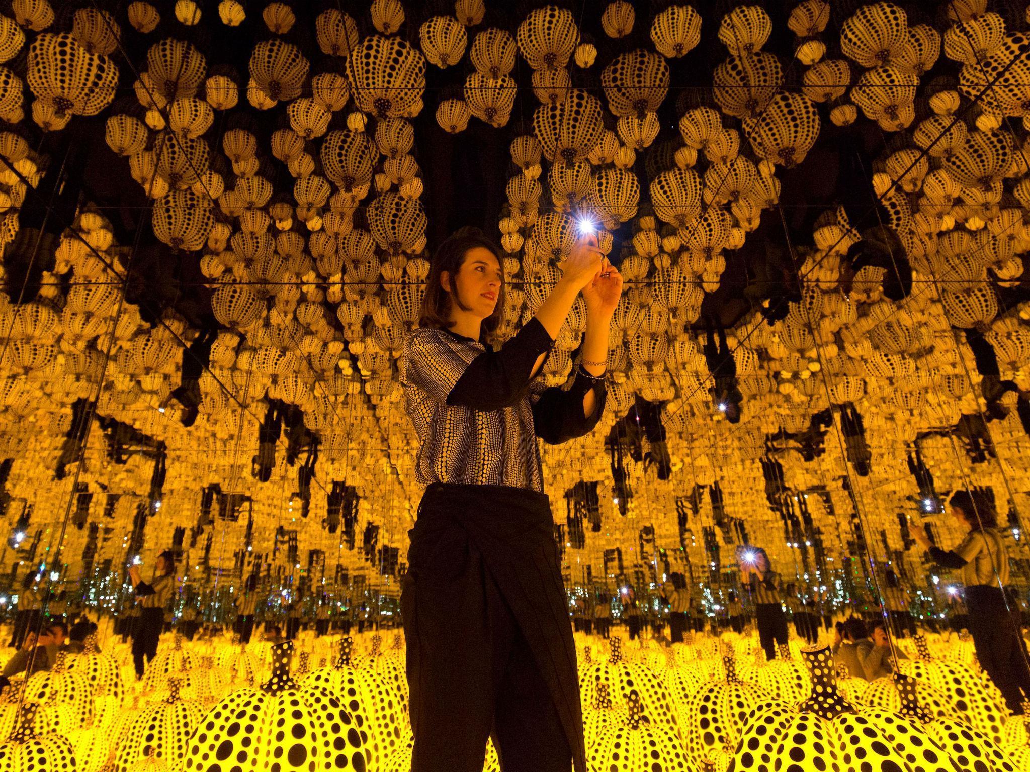A gallery assistant poses for a photo with 'All the Eternal Love I Have for the Pumpkins' by Yayoi Kusama